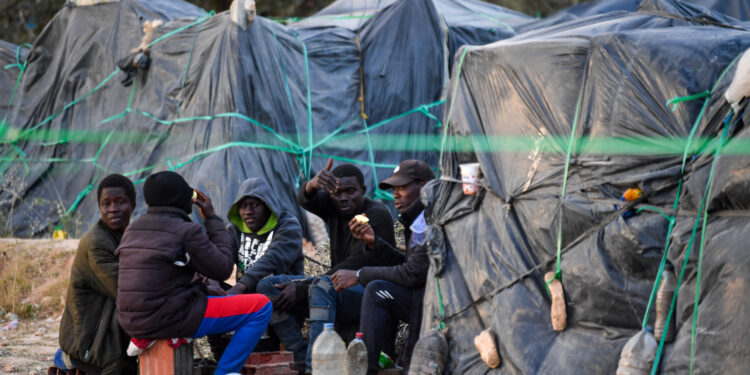 Migrants from sub-Saharan Africa sit next to makeshift shelters at a camp al-Amra on the outskirts of the Tunisian port city of Sfax on April 23, 2024. After President Kais Saied said in a speech last year that "hordes of illegal migrants" posed a demographic threat to Tunisia, anti-migrant violence broke out and hundreds of sub-Saharan Africans were kicked out of their jobs and homes. (Photo by Fethi Belaid / AFP)